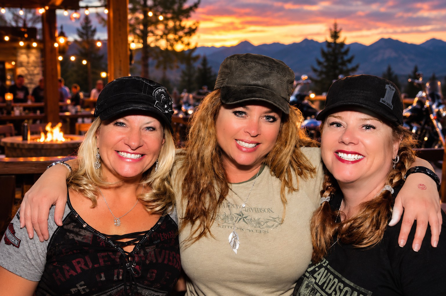 Three women smiling together with mountains and a sunset behind them